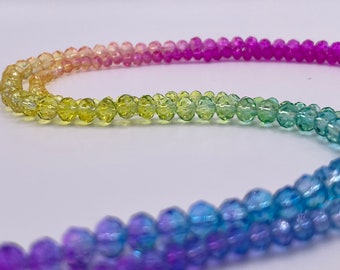 May include: A rainbow-coloured beaded necklace with faceted glass beads. The beads are arranged in a gradient from pink to yellow to blue to purple.
