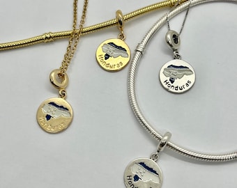 May include: Two silver and one gold charm bracelets with a Honduras charm on each. The charms are round and feature a white outline of the country of Honduras with a blue map inside. The word "Honduras" is written in gold lettering below the map.