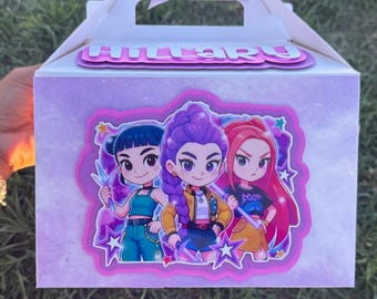 May include: A white gable box with a handle and a purple bow. The box features a cartoon graphic of three girls with different hair colors and outfits. The name "HILLARY" is printed on the top of the box.