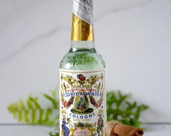 Pode incluir: Uma garrafa de vidro transparente de colônia Florida Water com tampa e rótulo de folha de ouro. O rótulo apresenta ilustrações florais e botânicas com o texto "MURRAY & LANMAN FLORIDA WATER COLOGNE NEW YORK". A garrafa tem 221 ml.