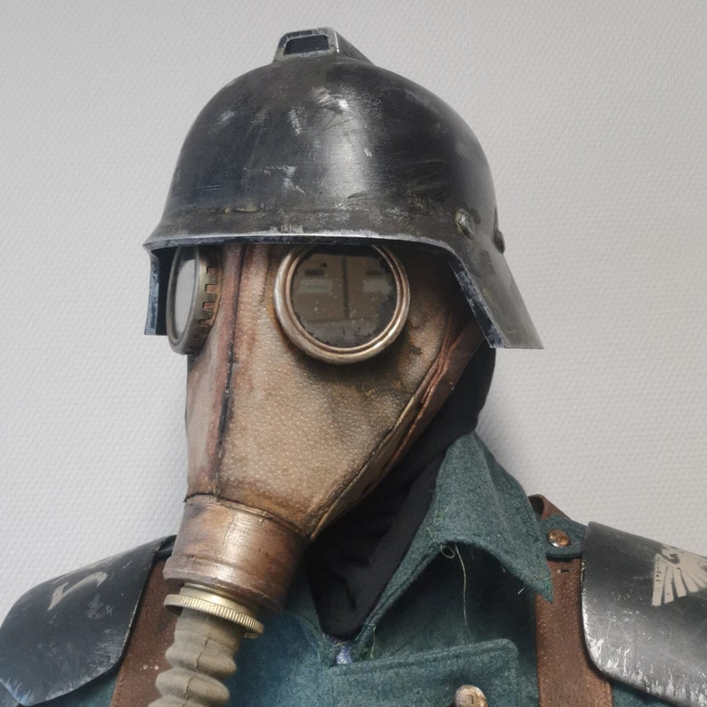 May include: A black helmet with a gas mask attached. The helmet has a worn, distressed look and the gas mask is made of brown leather with two round glass lenses.