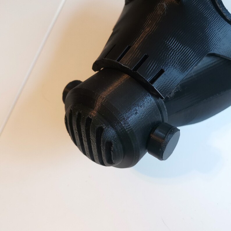 May include: A black 3D printed gas mask with a textured surface and a round, ribbed mouthpiece.