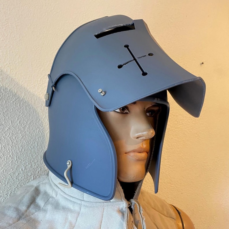 May include: A blue medieval helmet with a cross design on the visor. The helmet has a curved brim and a hinged side piece. The helmet is displayed on a mannequin.