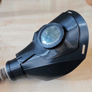 K&ouml;nnte beinhalten: Eine schwarze Plastikgasmaske mit einer klaren Plastiklinse. Die Maske hat einen Schlauch.