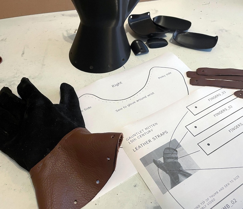 May include: A black suede glove with a brown leather cuff, a black 3D-printed gauntlet component, several small black plastic plates, brown leather straps, and printed instructional diagrams labelled Gauntlet Mitten 15th Century.