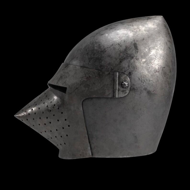 Pode incluir: Um capacete medieval de a&ccedil;o com viseira pontiaguda e topo arredondado. A viseira tem pequenos orif&iacute;cios de ventila&ccedil;&atilde;o e uma fenda estreita para a vis&atilde;o. O capacete &eacute; de cor cinza met&aacute;lico escuro.