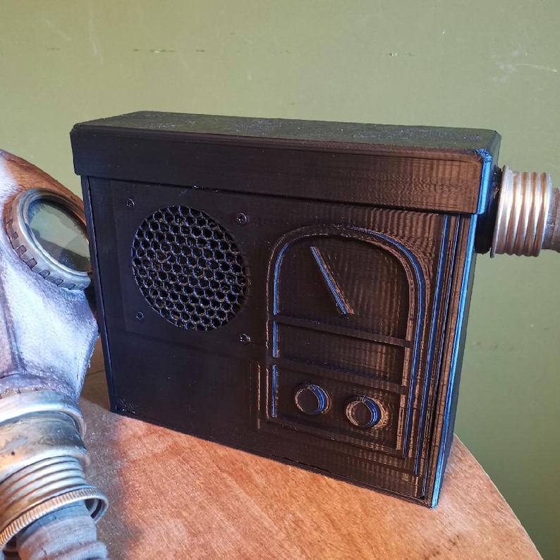 May include: A black 3D printed box with a speaker grill, a dial, and two knobs. The box has a vintage radio design.
