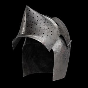 Pode incluir: Um capacete de a&ccedil;o desgastado com viseira pontiaguda e numerosos pequenos orif&iacute;cios de ventila&ccedil;&atilde;o. A superf&iacute;cie do capacete mostra sinais de desgaste e tem um acabamento met&aacute;lico escuro. O design sugere um tema hist&oacute;rico ou medieval.