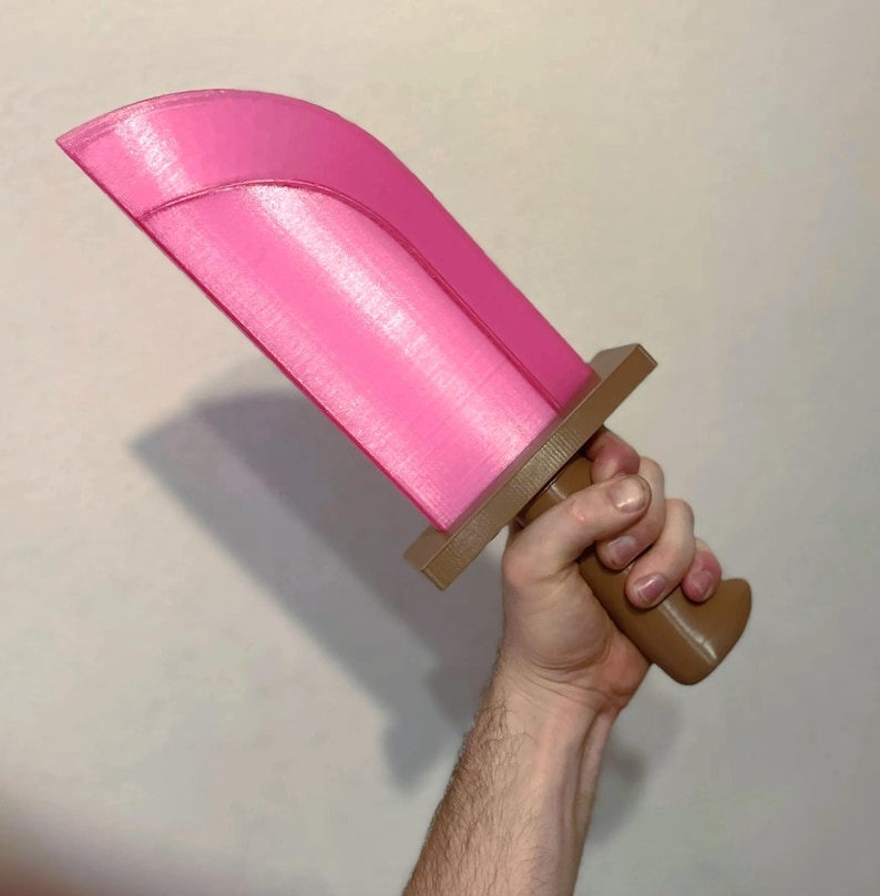 May include: A pink toy sword with a brown handle and crossguard. The blade is a vibrant pink, and the handle is a contrasting brown. The sword is held in a hand against a plain background.
