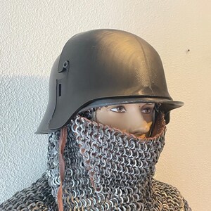 May include: A dark gray helmet with a visor and side details, worn over a chainmail coif. The helmet is displayed on a mannequin head. The chainmail covers the neck and shoulders, with leather straps visible.