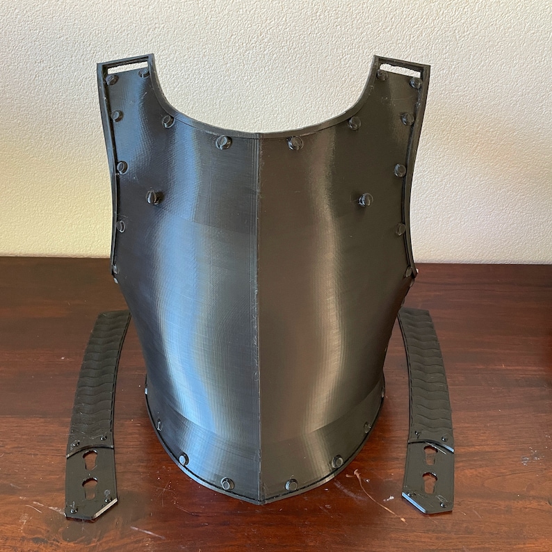 Op de afbeelding: Een zwart 3D-geprint borststuk van een harnas met twee afzonderlijke zwarte 3D-geprinte schouderbanden.