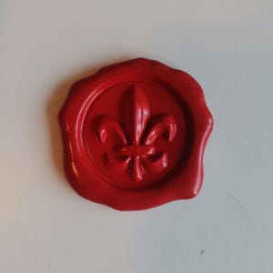 Może przedstawiać: Czerwona pieczęć woskowa z wzorem lilii.