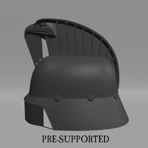 Puede incluir: Un modelo impreso en 3D de un casco con una cresta de &aacute;guila. El casco es gris y tiene una visera. El texto "PRE-SUPPORTED" est&aacute; impreso debajo del casco.