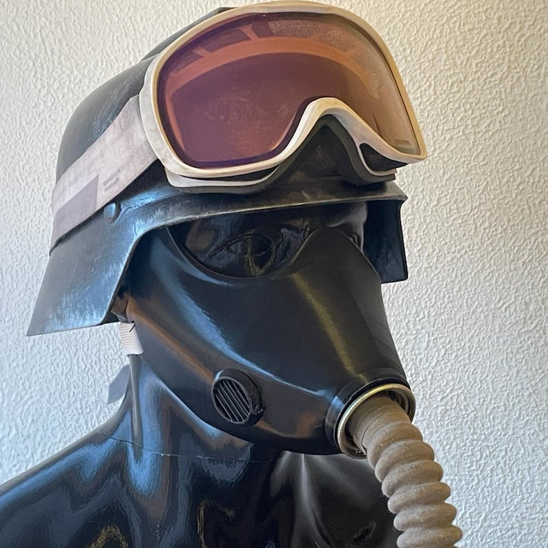 May include: A black gas mask with a white and gray ski goggle helmet. The gas mask has a black rubber mouthpiece and a brown hose.