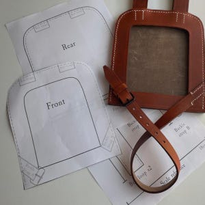 May include: Leather pattern pieces for a bag with instructions for cutting and assembling. The pattern includes two pieces labeled "Front" and "Rear" and a strap with a buckle.