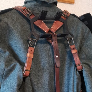 May include: A black metal frame with brown leather straps and buckles. The straps are adjustable and can be worn over the shoulders. The frame is designed to hold a variety of items, such as a camera or other equipment.