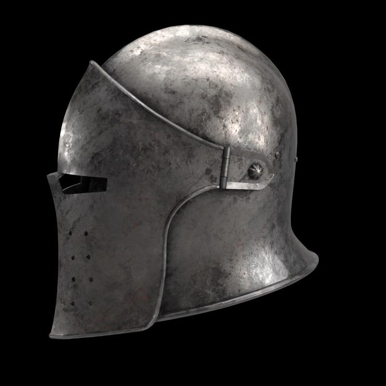 May include: A weathered, metallic helmet with a visor and a rounded top. The helmet has a dark, aged appearance, suggesting historical use. The visor features a horizontal eye slit and several small ventilation holes.