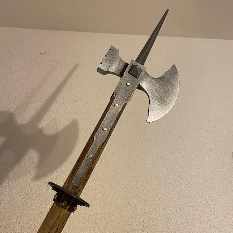 Op de afbeelding: Een middeleeuwse strijdbijl met een houten schacht, metalen blad en punt. De bijlkop heeft een gebogen blad en een hamerachtig uitsteeksel. De metalen componenten hebben een zilveren afwerking en de houten schacht is lichtbruin.