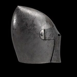 May include: A medieval steel helmet with a pointed top and a visor. The helmet is a dark, metallic gray color and has a riveted visor. The design suggests it was used for protection in combat.