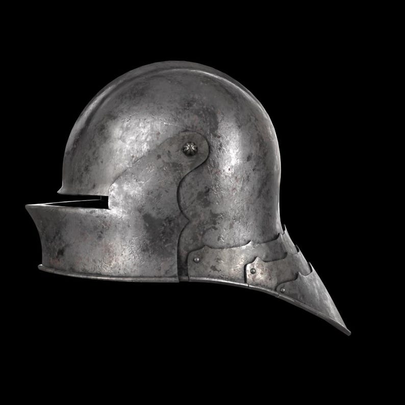 May include: A steel helmet with a rounded top and a visor. The helmet has a pointed lower edge and is riveted together. The metal has a slightly weathered appearance, suggesting age or use. The helmet is set against a black background.