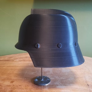 May include: A black plastic helmet with a smooth, textured surface. The helmet has a rounded top and a wide brim. There are three small, round, black accents on the side of the helmet.