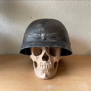 May include: A black helmet with a skull and wings design on the front. The helmet is sitting on top of a white skull.