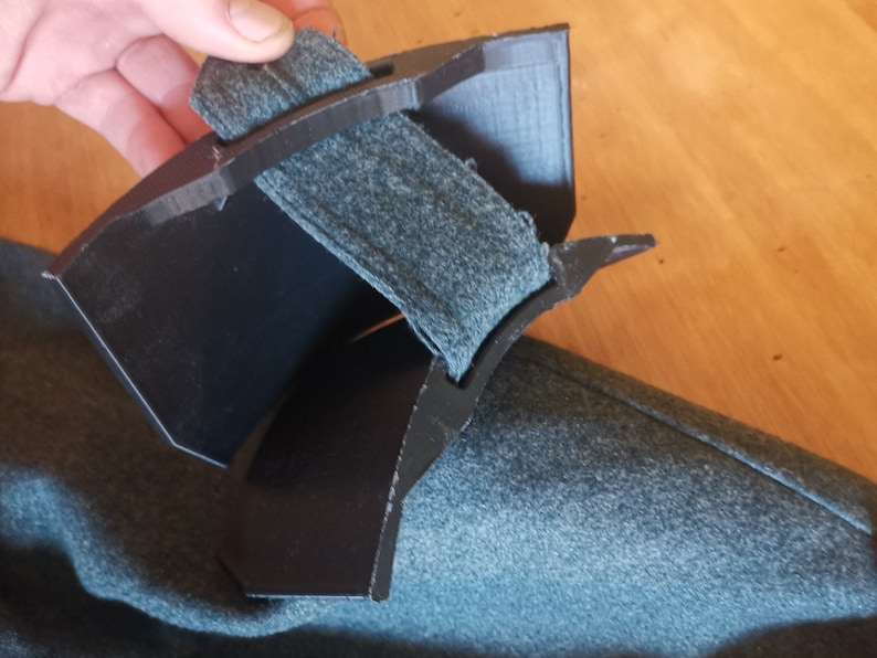 May include: A black plastic object with a gray fabric strap. The object is curved and has a textured surface.