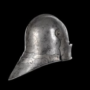 May include: A medieval steel helmet with a pointed visor and a curved, rounded top. The helmet has riveted plates around the neck and a small opening for the eyes. The metal has a worn, aged appearance.