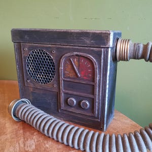 May include: A dark brown wooden box with a metal grill, a gauge, and two knobs. A gray hose is attached to the side of the box.