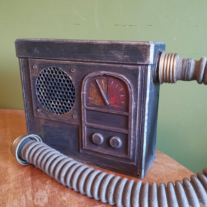 May include: A dark brown wooden box with a metal grill, a gauge, and two knobs. A gray hose is attached to the side of the box.