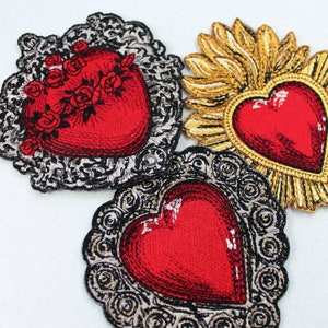Puede incluir: Tres parches bordados para planchar que presentan corazones rojos con marcos ornamentados. Los corazones est&aacute;n rodeados de bordados dorados, plateados y negros.