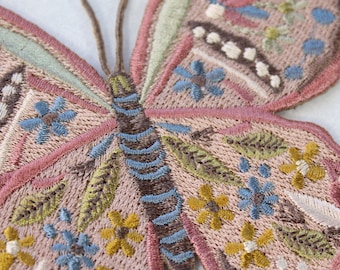 May include: A pink and brown embroidered butterfly with blue, green, and yellow floral details. The butterfly is a decorative patch or applique.