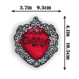 Puede incluir: Coraz&oacute;n rojo bordado con una corona de flores, rodeado de un marco adornado en negro y plata. El coraz&oacute;n mide 9,3 cm de ancho y 10,5 cm de alto.