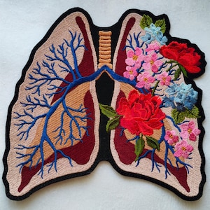 Könnte beinhalten: Gestickter Aufnäher eines menschlichen Lungenflügels mit detailliertem anatomischen Design, umgeben von bunten Blumen in den Farben Rosa, Rot, Blau und Grün.