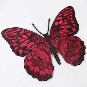 May include: Embroidered butterfly patch in shades of red and burgundy. The butterfly has detailed wing patterns and a brown body and antennae. This decorative patch can be sewn or ironed onto fabric.