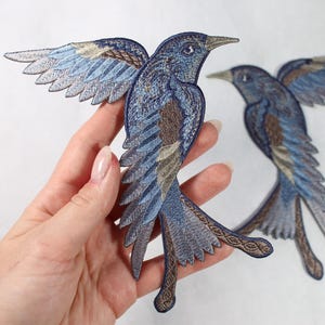 Puede incluir: Parches bordados de pájaros en tonos azules, marrones y beige. Los parches presentan diseños detallados de alas y cola, con un pájaro en pose de vuelo. Los parches son probablemente para uso decorativo en ropa o accesorios.