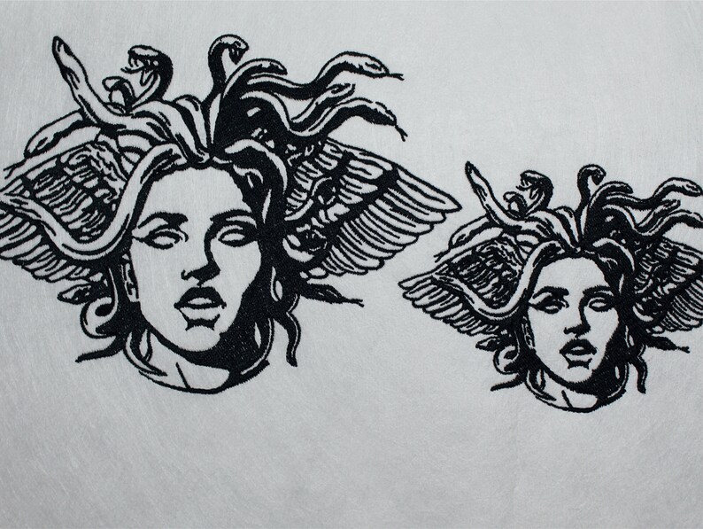 May include: Two black and white Medusa head designs. The larger design features a detailed depiction of Medusa's face with snakes for hair and feathered wings. The smaller design is a similar, but smaller, version of the same image.