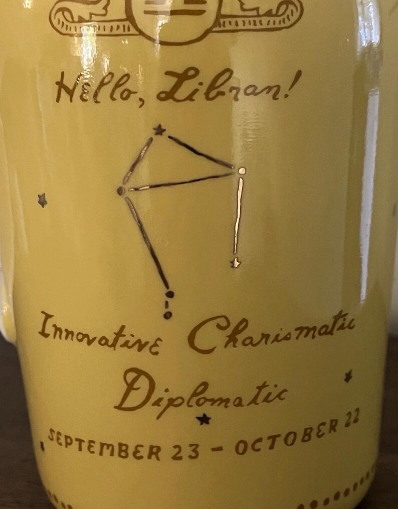 May include: A yellow ceramic mug with the text "Hello, Libran!" and the Libra constellation in dark brown. Additional text includes "Innovative, Charismatic, Diplomatic" and "September 23 - October 22".