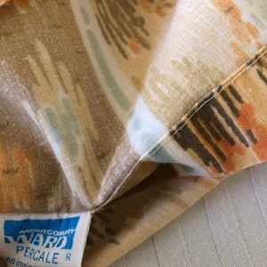 May include: Close-up of a patterned fabric with a tag. The fabric features a design in shades of brown, tan, orange, and blue. The tag reads "MONTGOMERY WARD PERCALE R no ironing needed."