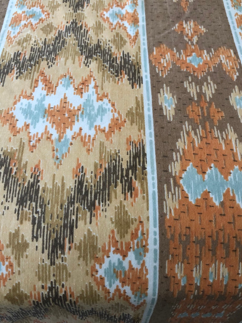 May include: Close-up of a fabric with a repeating geometric pattern. The design features vertical stripes and a mix of colours, including tan, brown, black, and light blue. The pattern has a textured appearance.