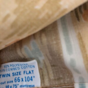 May include: Twin size flat sheet with a beige, brown, and light blue abstract pattern. The label indicates it is made of 50% polyester and 50% combed cotton. The cut size is 168 x 264 cm, designed for a 99 x 190 cm mattress.