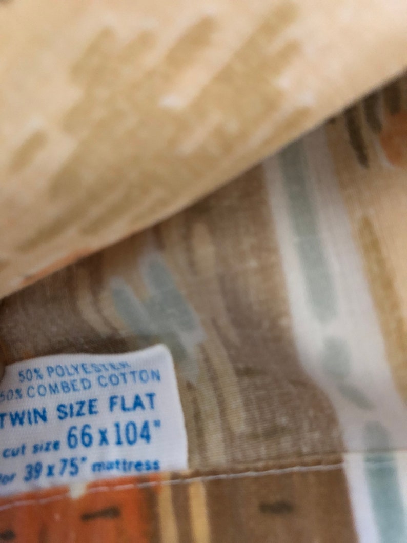 May include: Twin size flat sheet with a beige, brown, and light blue abstract pattern. The label indicates it is made of 50% polyester and 50% combed cotton. The cut size is 168 x 264 cm, designed for a 99 x 190 cm mattress.
