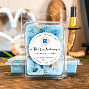May include: A blue soy wax melt in a clear plastic container with a label that reads "CESARAH'S SPOOKY SHOP ~ Third Eye Awakening ~ JUNIPER BERRY & EUCALUYPTUS HAND-POURED IN GEORGIA 3 OZ 85 GM ALL-NATURAL SOY WAX MELT". The label features a blue and white evil eye symbol.