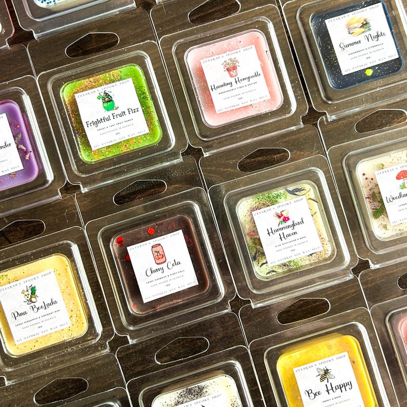 May include: A collection of wax melts in clear plastic containers. The wax melts are square shaped and have various scents and designs. Some of the scents include "Frightful Fruit Fizz", "Hunting Honeyuckle", "Summer Nights", "Pina Beefada", "Cherry Cola", "Hummingbird Haven", "Woodland", and "Bee Happy".