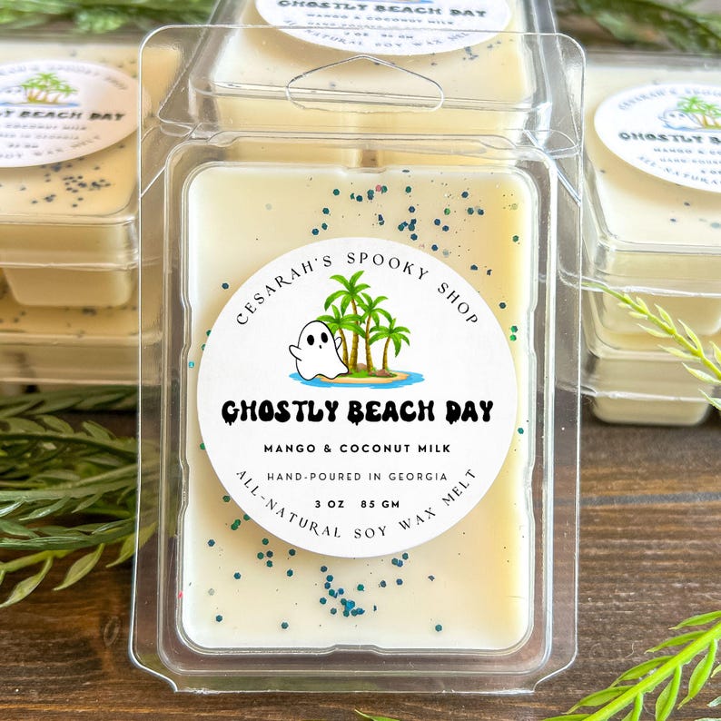 May include: A clear plastic container holding a wax melt with the text "Ghostly Beach Day." The wax is a light yellow color with blue glitter. The label features a ghost, palm trees, and the words "Mango & Coconut Milk."