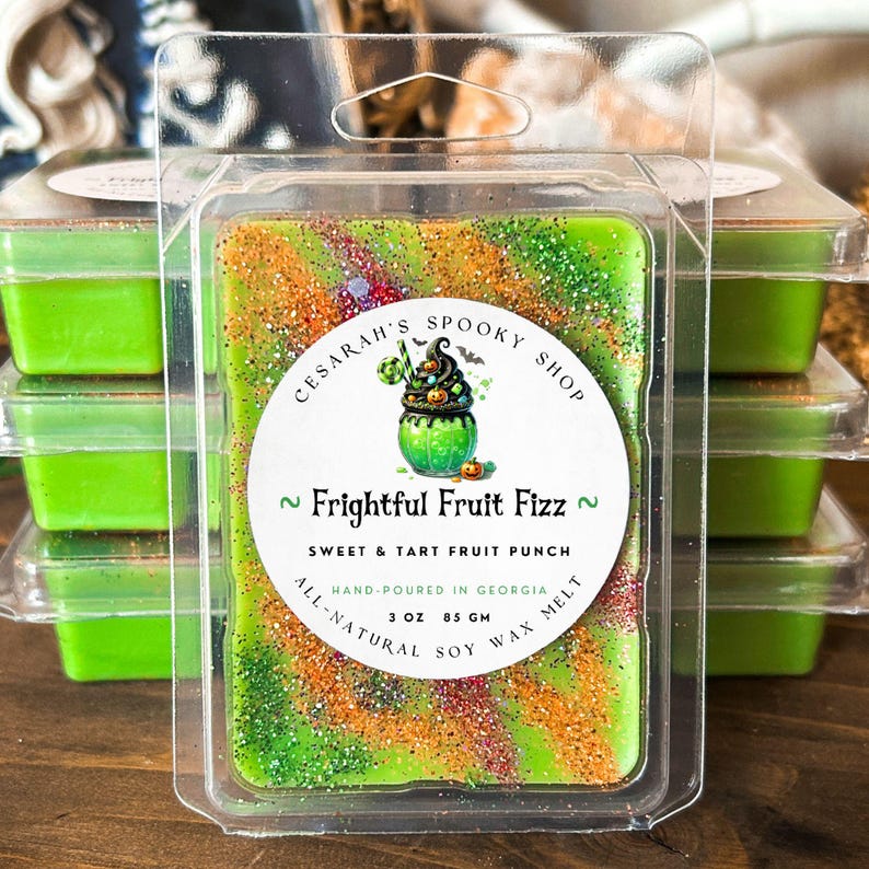 May include: A green wax melt with orange and gold glitter, labeled "Frightful Fruit Fizz" with a Halloween-themed graphic. The packaging states it is hand-poured in Georgia, made of all-natural soy wax, and weighs 3 oz (85 g).