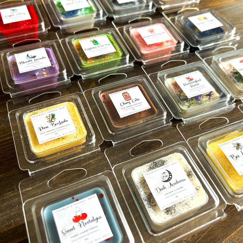 May include: Assortment of wax melts in clear plastic containers. The wax melts are in various colors and have different scents, including "Sweet Nostalgia", "Dark Academia", "Cherry Cola", "Pina Colada", "Moonlight Jasmine", "Hummingbird Nectar", "Bee Happy", and "Edible Fruit Pie".