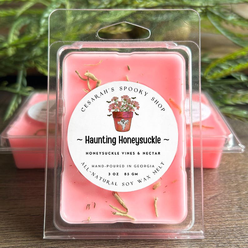 May include: A pink wax melt in a clear plastic clamshell. The label reads "Haunting Honeysuckle" with a floral illustration. The product is 3 oz (85 g) of all-natural soy wax, hand-poured in Georgia.
