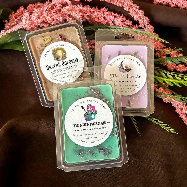 May include: Three wax melt packages from Cesarah's Spooky Shop. The scents are Secret Gardens, Moonlit Lavender, and Twisted Mermaid. Each package is in a clear plastic container with a label. The Twisted Mermaid melt is green with glitter.