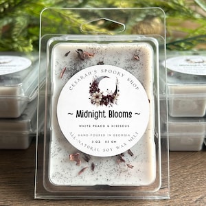 May include: A white wax melt with the text "Midnight Blooms" and "White Peach & Hibiscus." The label also reads "Hand-poured in Georgia" and "3 oz 85 gm." The wax melt is in a clear plastic container.